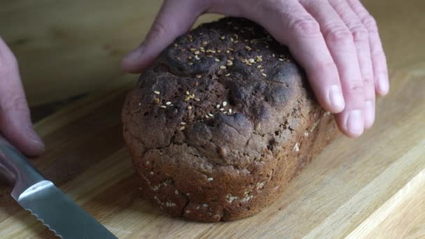 木製のまな板に黒パンの切断スライス ナイフで全粒穀物パンをカット 暗いパン 健康的なライフスタイルの終わり — ストック動画