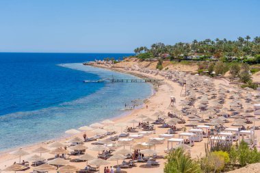 Sharm El Sheikh, Mısır - 25 Mayıs 2021: İnsanlar Sharm El Sheikh, Mısır, Afrika 'daki Kızıldeniz kıyısındaki bir tropik tatil beldesinde plaj sandalyeleri ve saman şemsiyeleriyle lüks bir kumsalda dinleniyorlar.