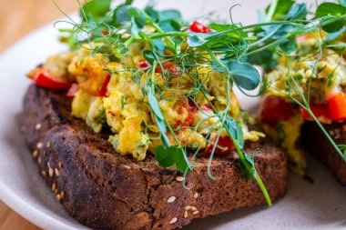 Sabah kahvaltısı sandviçi ve çırpılmış yumurta. Yumurtalı, peynirli, domatesli, kırmızı biberli ve bezelyeli sandviç. Omletli sandviçi kapat.
