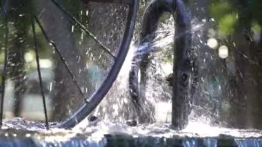Güneşli bir günde Batumi şehrinde su sıçrayan güneş ışığına karşı güzel bir çeşme ve bisiklet tekerleği, Georgia. Ağır çekim, yakın çekim.