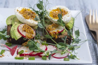 Ekmek tostu, haşlanmış yumurta, avokado dilimi, bezelye mikroçerezi ve taze turp bir kafede, yakın plan kahvaltı zamanı.