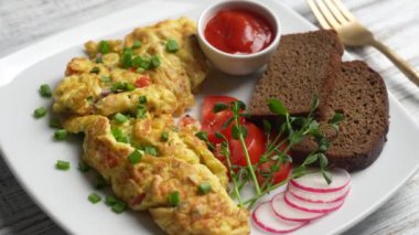 Beyaz ahşap zemin üzerinde soğan, domates, biber, yumurta ve peynirle doldurulmuş omlet ve çatal. Kahvaltı için sağlıklı diyet yemeği. Lezzetli sabah yemeği. Üst görünüm, kapat, döndür