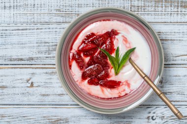 Kırmızı çilekli beyaz tabak ve ahşap bir masada yoğurt, yakın çekim, üst manzara