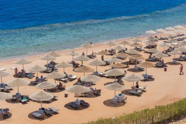 Sharm El Sheikh, Mısır - 25 Mayıs 2021: İnsanlar Sharm El Sheikh, Mısır, Afrika 'daki Kızıldeniz kıyısındaki bir tropik tatil beldesinde plaj sandalyeleri ve saman şemsiyeleriyle lüks bir kumsalda dinleniyorlar.