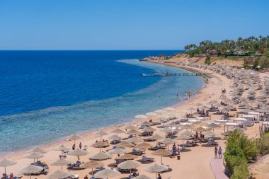 Sharm El Sheikh, Mısır - 25 Mayıs 2021: İnsanlar Sharm El Sheikh, Mısır, Afrika 'daki Kızıldeniz kıyısındaki bir tropik tatil beldesinde plaj sandalyeleri ve saman şemsiyeleriyle lüks bir kumsalda dinleniyorlar.