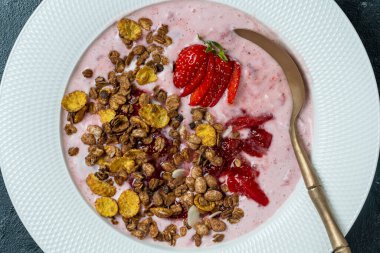 Kırmızı çilekli beyaz tabak, granola ve siyah arka planda doğal yoğurt, yakın plan, üst manzara