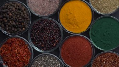 Arka planda farklı baharatlar ve bitkiler dönüyor, yakın plan, üst görünüm. Renkli baharatlar, tohumlar ve yemek pişirmek için bitkiler.