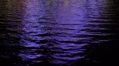 Gece deniz dalgaları parlak cadde ışıklarını yansıtıyor. Yaklaş.