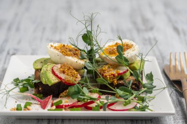 Ekmek tostu, haşlanmış yumurta, avokado dilimi, bezelye mikroçerezi ve taze turp bir kafede, yakın plan kahvaltı zamanı.