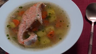 Fresh salmon fish soup with carrots, potatoes and herbs in a white plate, close up, rotates.Tasty dinner consists of a fish soup with salmon