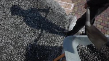 İşçi küreği bir el arabasına moloz koyar, yaklaşır. Küreğin yardımıyla el arabasına ezilmiş taşlar yükleyen adam. Kendi ellerinle inşa et.