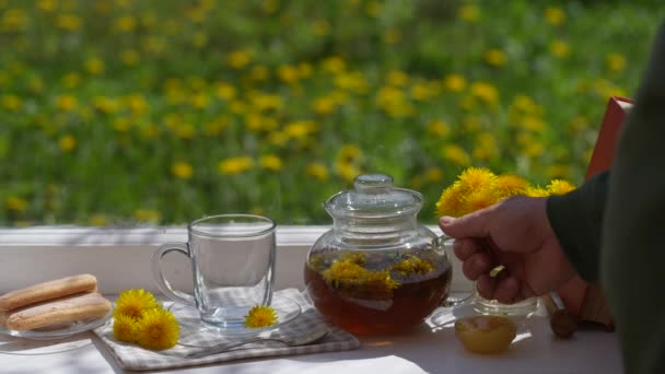 在自家花园附近的窗台上放着蜂蜜的新鲜蒲公英花中提取出美味的草茶 关上门 复制空间 玻璃杯茶壶里的热蒲公英茶倒入杯子里 — 图库视频影像
