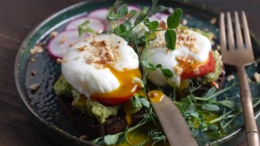 Bread toast, poached eggs, avocado pulp, pea microgreens  and fresh vegetables on plate in cafe, close up, rotates, breakfast time