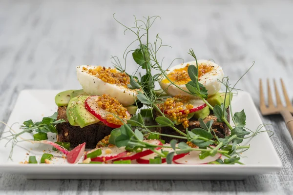 Ekmek tostu, haşlanmış yumurta, avokado dilimi, bezelye mikroçerezi ve taze turp bir kafede, yakın plan kahvaltı zamanı.