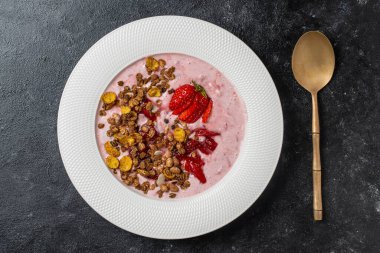 Kırmızı çilekli beyaz tabak, granola ve siyah arka planda doğal yoğurt, yakın plan, üst manzara