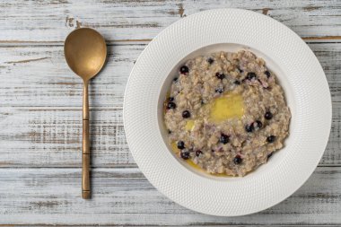 Yulaf ezmeli yulaf lapası, yaban mersini, tereyağı ve bal beyaz tabakta ahşap masada, yakın plan, üst manzara. Sağlıklı kahvaltı ve düzgün beslenme kavramı.