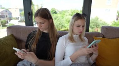 İki genç kız akıllı telefon kullanarak sosyal medyada geziniyor, haberleri kontrol ediyor, mobil oyunlar oynuyor ya da kanepede oturmuş mesaj yazıyor, kapatıyorlar.