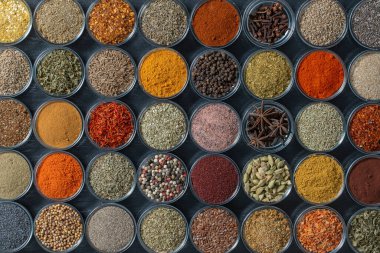 Arka planda yemek pişirmek için aromatik baharatlar, tohumlar ve kuru otlar küçük cam kaselerde, yakın plan, üst görüş