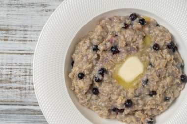Yulaf ezmeli yulaf lapası, yaban mersini, tereyağı ve bal beyaz tabakta ahşap masada, yakın plan, üst manzara. Sağlıklı kahvaltı ve düzgün beslenme kavramı.