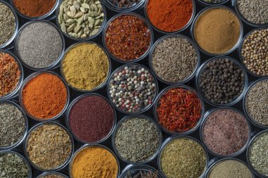 Arka planda yemek pişirmek için aromatik baharatlar, tohumlar ve kuru otlar küçük cam kaselerde, yakın plan, üst görüş