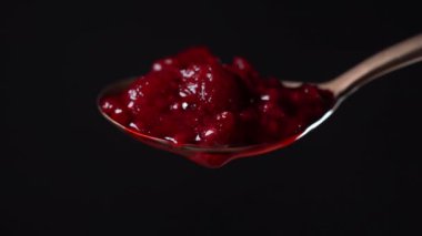 Kırmızı ahududu reçelli kaşık ve bir damla. Kırmızı ahududu reçeli siyah arka planda metal kaşıktan damlıyor ve aşağı akıyor. Yaklaş. Ev yapımı kırmızı ahududu reçelli pirinç kaşık.