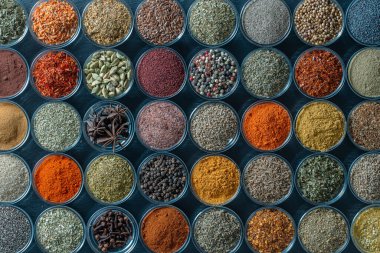 Arka planda yemek pişirmek için aromatik baharatlar, tohumlar ve kuru otlar küçük cam kaselerde, yakın plan, üst görüş