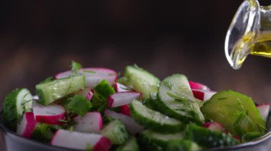 Pouring olive oil on healthy fresh vegetables salad, close up. Delicious vegetable diet salad of cucumber, radish, green onion, dill and olive oil. Concept healthy meal and mediterranean kitchen