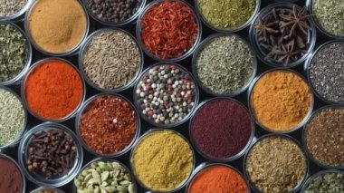 Arka planda yemek pişirmek için çeşitli aromatik baharatlar, tohumlar ve kuru otlar. Smal cam kaselerde dönüyorlar, kapatıyorlar, üstten bakıyorlar.