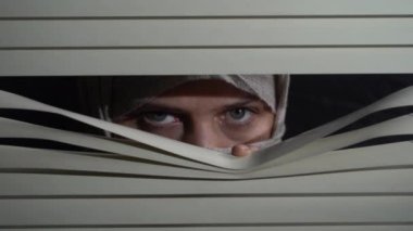 Kapalı alandaki başörtülü esmer kadının ön portresini kapat geceleri elleriyle pencereye panjur iterek. Dışarıdan korkunç görünüyor.