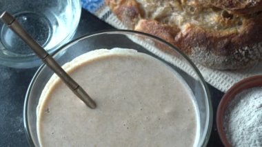 Mayasız mayalı ekmek, un, su ve hamur mayalı cam kavanoz. Ekmek, çörek, hamur işi ya da pizza için hamur mayası hazırlamak, yakın çekim, üst görünüm, döner