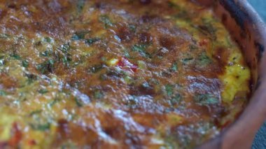 Ceramic bowl with vegetable frittata, simple vegetarian food. Frittata with tomato, pepper, onion and cheese on wooden table, close up. Italian egg omelette, rotates