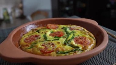 Sebzeli frittata ile seramik kase, basit vejetaryen yemeği. Yumurtalı frittata, domates, biber, soğan, peynir ve yeşil sarımsak yaprakları masada, döndür, kapat. Sağlıklı yumurta omleti.