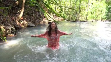Young woman in turquoise water of cascade waterfall at deep tropical rain forest, island Koh Phangan, Thailand, slow motion