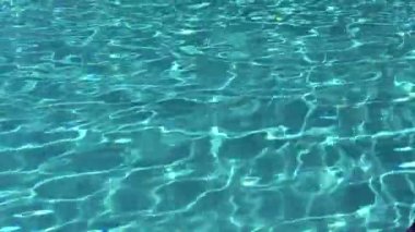 Mavi fayanslı yüzme havuzunda su dalgalanmaları. Mavi turkuaz havuz suyu. Güneş dalgalanmalarını aydınlatıyor. Aşağıda görünen fayanslar. Üst görünüm