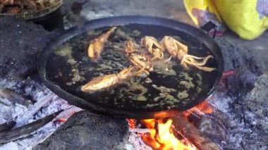 Satıcı, Doğu Afrika 'daki Tanzanya' nın Zanzibar adasındaki yerel bir sokak gıda pazarında büyük bir kızartma tavasında sebze yağında mürekkep balığı kızartıyor. Kapat.