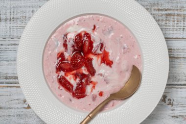 Kırmızı çilekli beyaz tabak ve ahşap bir masada yoğurt, yakın çekim, üst manzara