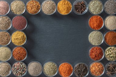 Arka planda yemek pişirmek için aromatik baharatlar, tohumlar ve kuru otlar küçük cam kaselerde, yakın plan, üst manzara. Metin için kopyalama alanı olan siyah sayfadaki baharat çeşitliliği