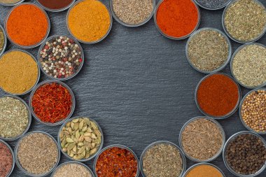 Arka planda yemek pişirmek için aromatik baharatlar, tohumlar ve kuru otlar küçük cam kaselerde, yakın plan, üst manzara. Metin için kopyalama alanı olan siyah sayfadaki baharat çeşitliliği