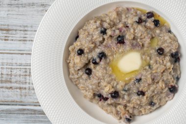 Yulaf ezmeli yulaf lapası, yaban mersini, tereyağı ve bal beyaz tabakta ahşap masada, yakın plan, üst manzara. Sağlıklı kahvaltı ve düzgün beslenme kavramı.