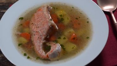 Fresh salmon fish soup with carrots, potatoes and herbs in a white plate, close up, rotates.Tasty dinner consists of a fish soup with salmon