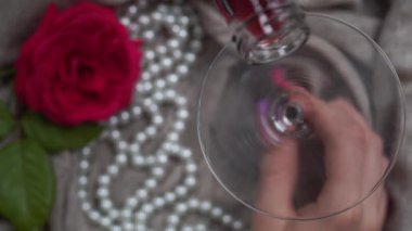 Genç beyaz bir kadın, zeytinli bir martini ile arka planda inci bir kolye ve kırmızı bir gül tutuyor. Yakın plan, üst manzara.