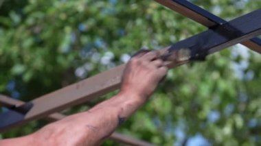 İnşaatçı metal profili siyah boyayla boyuyor, açık havada. Adam metali boyamak için fırça tutuyor. Ev geliştirme ve DIY konsepti. Metal kare boruların paslanma ve aşınmadan korunması