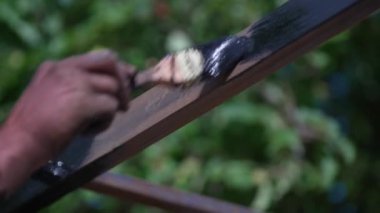 İnşaatçı metal profili siyah boyayla boyuyor, açık havada. Adam metali boyamak için fırça tutuyor. Ev geliştirme ve DIY konsepti. Metal kare boruların paslanma ve aşınmadan korunması