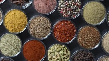 Arka planda yemek pişirmek için çeşitli aromatik baharatlar, tohumlar ve kuru otlar. Smal cam kaselerde dönüyorlar, kapatıyorlar, üstten bakıyorlar.