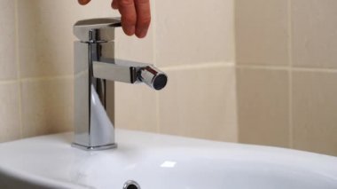 Modern banyodaki bej kaplamalı musluktan akan su ile birlikte beyaz seramik bidet detayları. Basit stil ve modern ev dekorasyonu. Kapat.