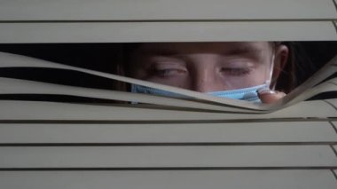 İçerideki koruyucu maskeli genç kızın ön portresini kapat. Pencere perdelerini elleriyle it. Geceleri korkusuzca dışarı bakıyorum.