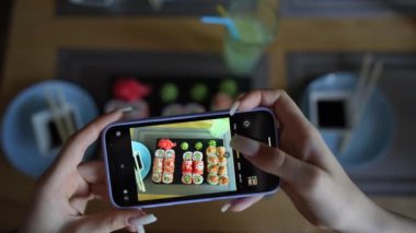 Kız, rahat Japon restoranında akıllı telefon kullanarak suşi fotoğrafı çekiyor. Kadın eli, modern akıllı telefonla yiyeceklerin fotoğrafını çeker. Yaklaş, 4K