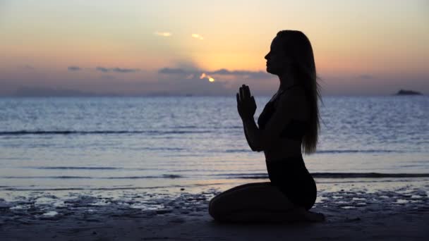 夕暮れ時にはトロピカルビーチのヨガポーズで座っている女性のシルエット 白人の女の子練習ヨガ近く海の水 — ストック動画