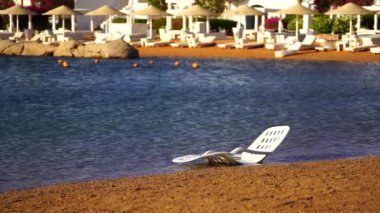 Mısır 'ın Sharm El Sheikh kentindeki tropikal bir plajda deniz suyunun yanında beyaz plastik güneş uzanır. Seyahat ve doğa kavramı