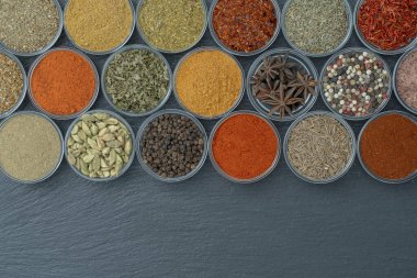 Arka planda yemek pişirmek için aromatik baharatlar, tohumlar ve kuru otlar küçük cam kaselerde, üst görünümü kapat, boşluğu kopyala